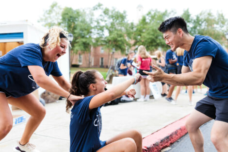 Two students help a third student during a game at Orientation. All have broad smiles.