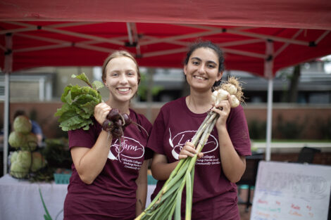 Two students smile with produce.